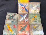 Plusieurs petits avions en plastique sont exposés dans une vitrine posée sur une surface noire.