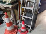 une échelle appuyée contre un mur, à côté d'une pile de cônes de signalisation