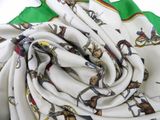 a close up of a white and green scarf with a picture of horses on it