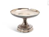 une petite assiette en argent posée sur un socle, sur fond blanc