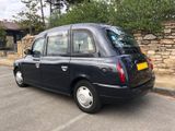 the black taxi is parked in the parking lot next to a stone wall