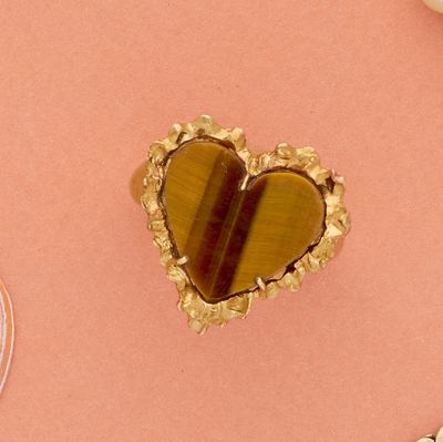 une broche en forme de cœur posée sur un fond rose, à côté d'autres objets