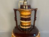 a brown and yellow vase on a stand with a cup on top