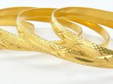 trois bracelets en or posés sur une surface blanche, sur fond blanc