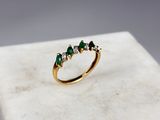 un gros plan d'une bague en or sertie de pierres vertes posée sur une surface en marbre