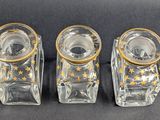 three glass candle holders with gold stars on them on a black surface