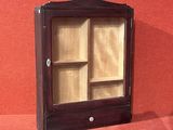 une petite armoire en bois avec une porte vitrée, posée contre un mur rouge