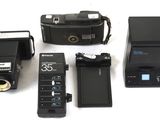 a camera, flash, camera case, and other electronic equipment laid out on a white surface