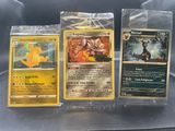 Trois cartes Pokémon sont rangées dans des pochettes en plastique posées sur une table