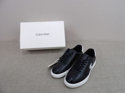 des baskets en cuir noir à semelles blanches et une boîte posée par terre