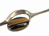 silver spoon with a tiger eye stone in it on a white surface