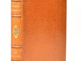 an old book with a brown leather cover sitting on a white surface