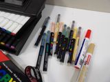 many pens and markers sitting on a desk next to a box of markers