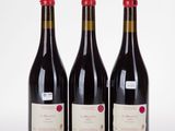 three bottles of red wine sitting next to each other on a white surface