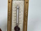 a gold frame with a thermometer on it next to a wooden object