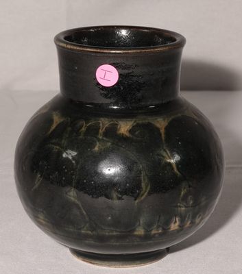 un vase noir sur lequel est collé un autocollant rose