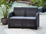 un canapé noir posé sur une terrasse, avec une plante en pot en arrière-plan