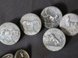 six ancient silver coins and a silver seal on a black surface