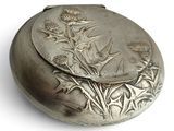 a silver pill case with a thistle design on it