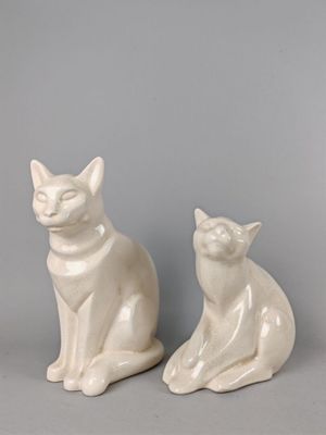 une paire de figurines de chats en céramique blanche posées sur une surface grise