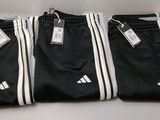 trois pantalons Adidas noirs avec des bandes blanches