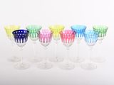 six verres à vin de couleurs différentes alignés sur une surface blanche