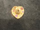 a gold heart shaped pin with pink and blue stones on it
