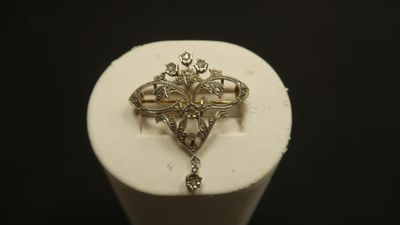 une photo d'une broche en forme de croix dorée posée sur un socle blanc