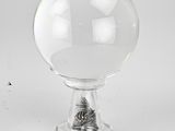 une boule en verre transparent posée sur un socle métallique, sur une surface blanche