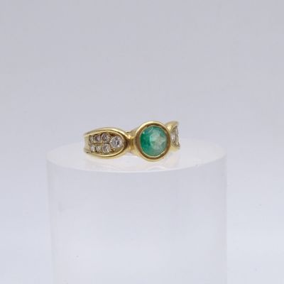 gros plan d'une bague en or avec une pierre verte et des diamants