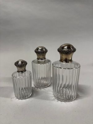 trois bouteilles en verre avec des bouchons argentés, posées sur une surface blanche