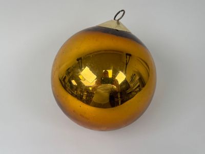 une boule de Noël jaune accrochée à un mur blanc, avec le reflet d'une personne dans le miroir