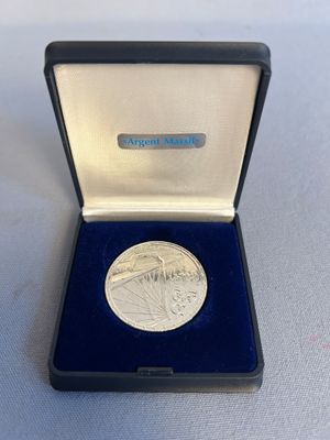 une photo d'une médaille d'argent dans un écrin bleu