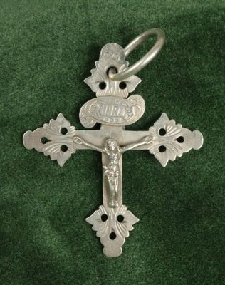 une croix en argent sur un tissu vert, avec un petit oiseau sur la croix