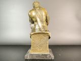 bronze statue of a man sitting on a pedestal with his back to the camera