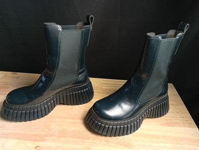 une paire de bottes noires posées sur une table en bois, avec un mur noir en arrière-plan