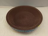 un bol marron et bleu posé sur une nappe blanche, sur fond blanc