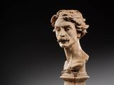 un buste sculpté représentant un homme moustachu, posé sur un socle
