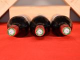three bottles of wine sit in a wooden crate on a red cloth