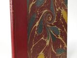 an old book with a red cover sitting on top of a white table