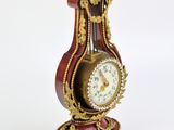 a red and gold clock on a stand on a white surface