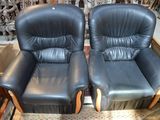 une paire de fauteuils inclinables en cuir noir, avec accoudoirs en bois et repose-pieds