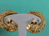 pair of gold tone earrings on a white stand against a turquoise background
