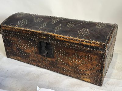 une boîte en bois ornée de rivets, posée sur une surface blanche