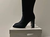 black high heeled boots sitting on top of a stack of white boxes
