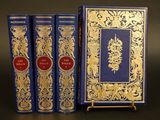 trois livres bleus ornés de motifs dorés, posés sur une table