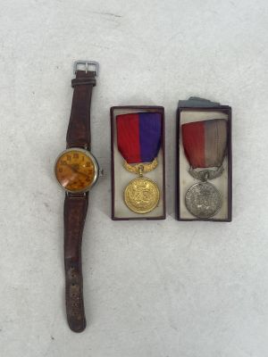 three medals and a watch sitting on top of a white surface