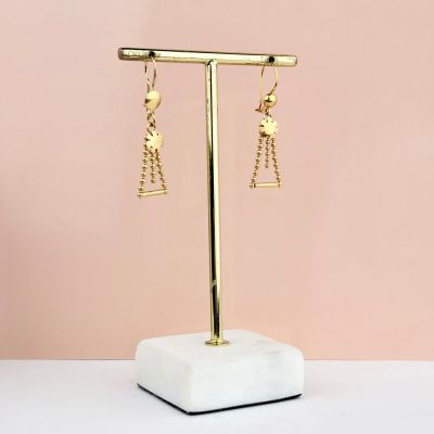 a pair of gold earrings on a stand against a pink wall