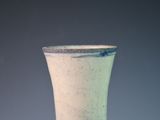 a green vase sitting on a table against a gray wall