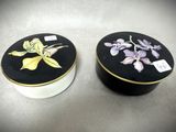 deux boîtes noires et blanches ornées de fleurs, posées sur une table